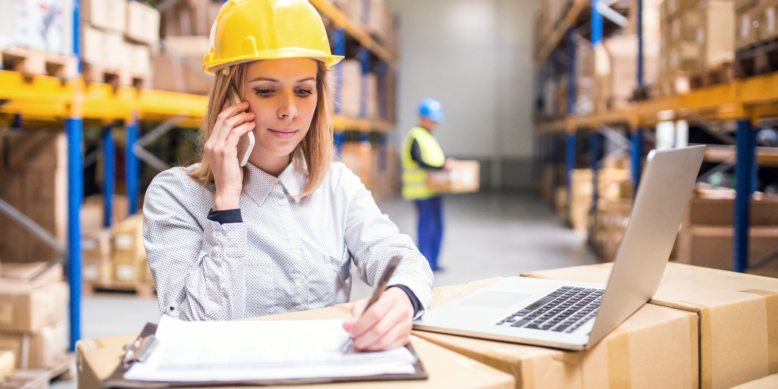 supply chain skills in action - a woman with a phone, laptop, and notebook in a warehouse